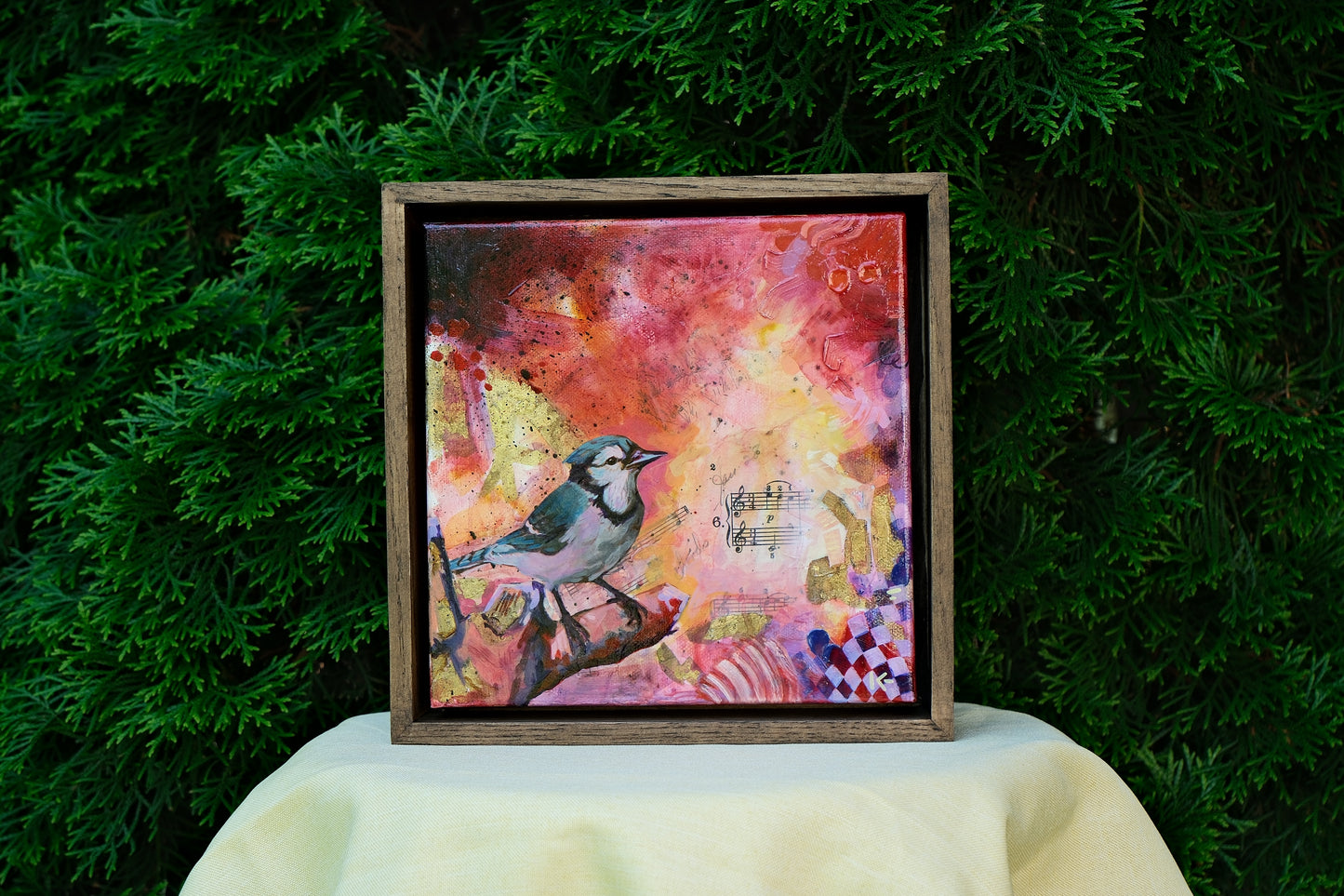 Framed artwork with a bird on a colorful background against a green leafy background
