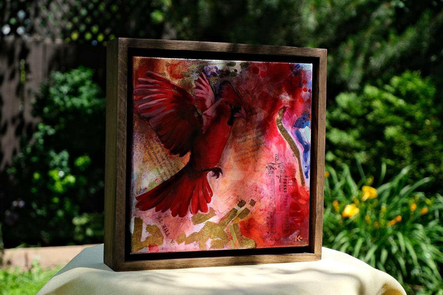 Framed artwork with a red bird and abstract design on a green outdoor background