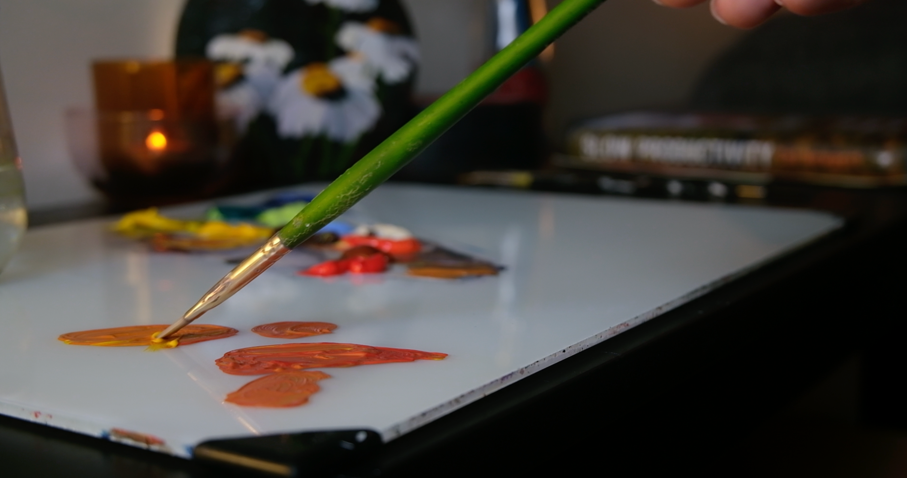 Person painting small orange shapes on a white surface with a green paintbrush.